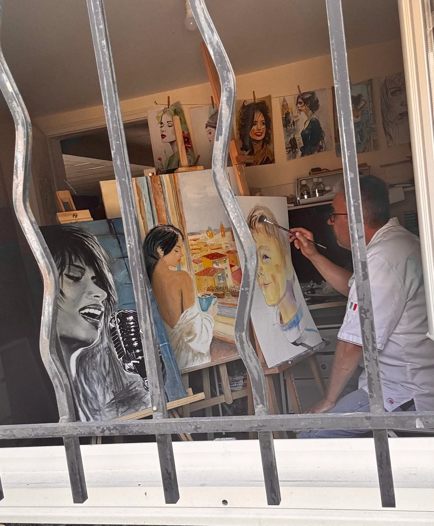 L'atelier vu depuis la rue : toiles en cours sur les chevalets et portraits accrochés au mur