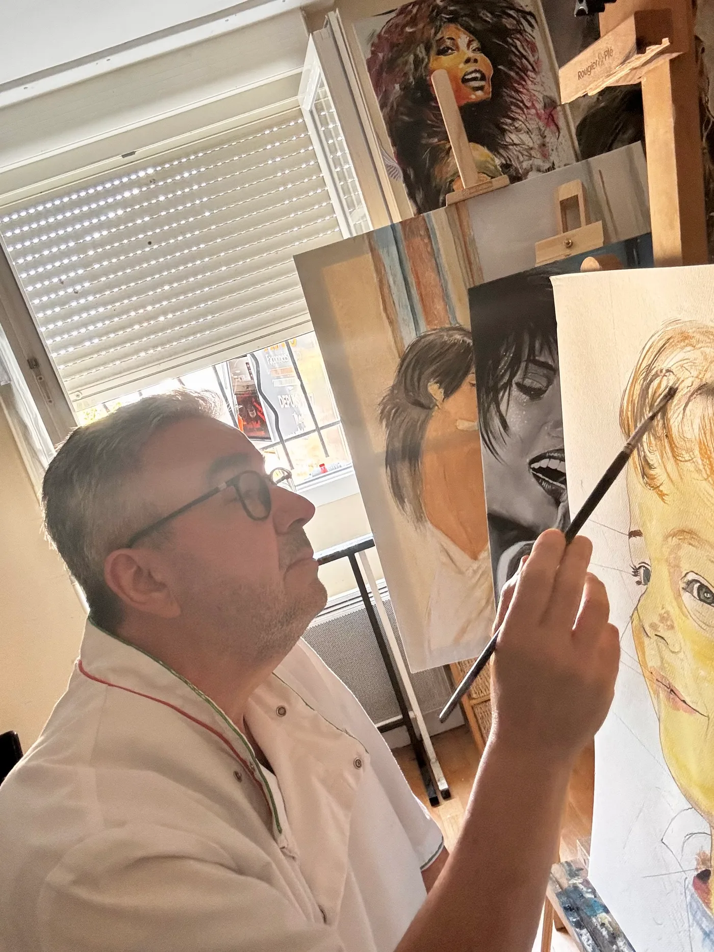 Michel Pesson, pinceau en main, peignant un portrait d'enfant sur le chevalet